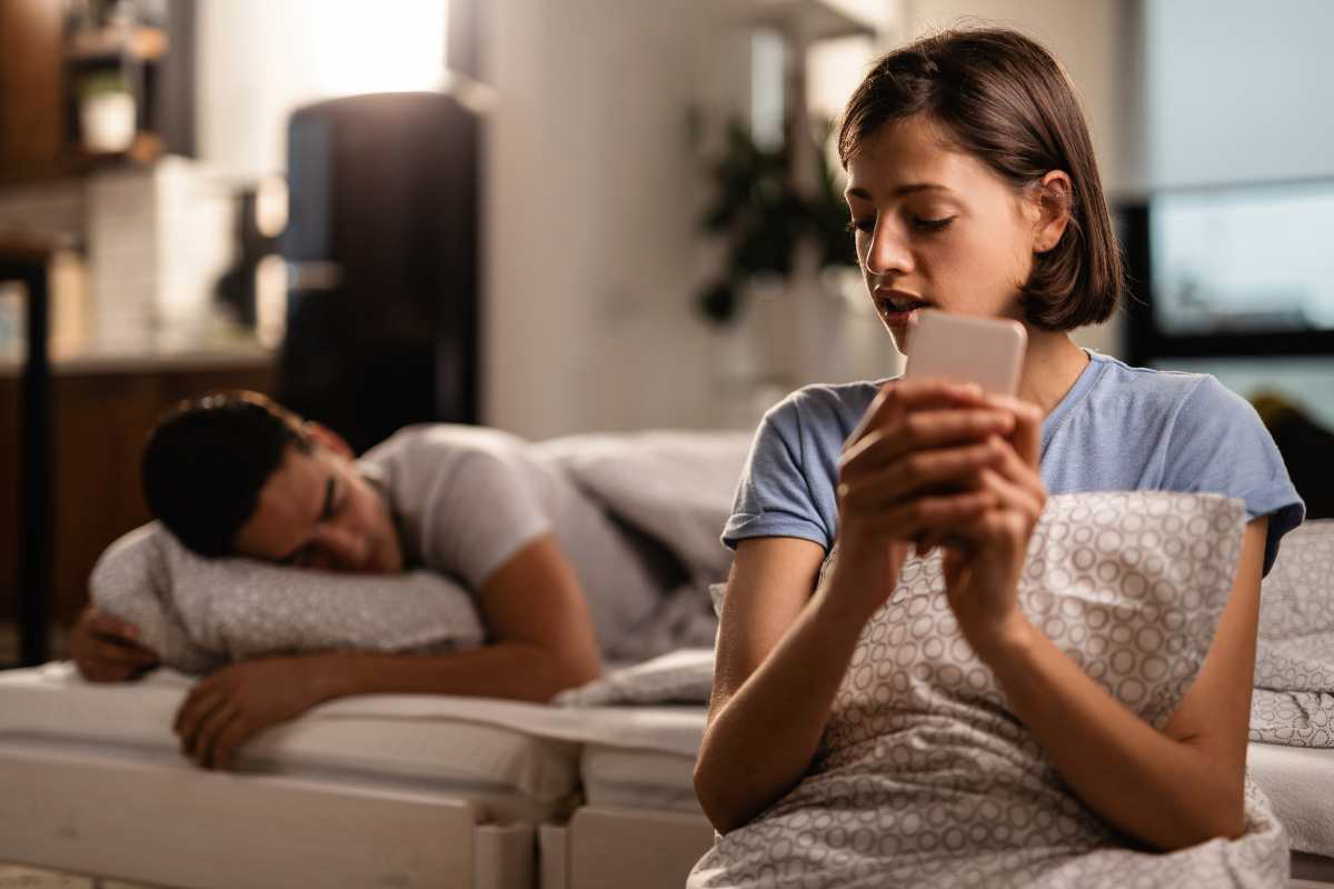 Una donna controlla il cellulare del compagno mentre dorme: è uno dei trucchi per scoprire un tradimento più utilizzati