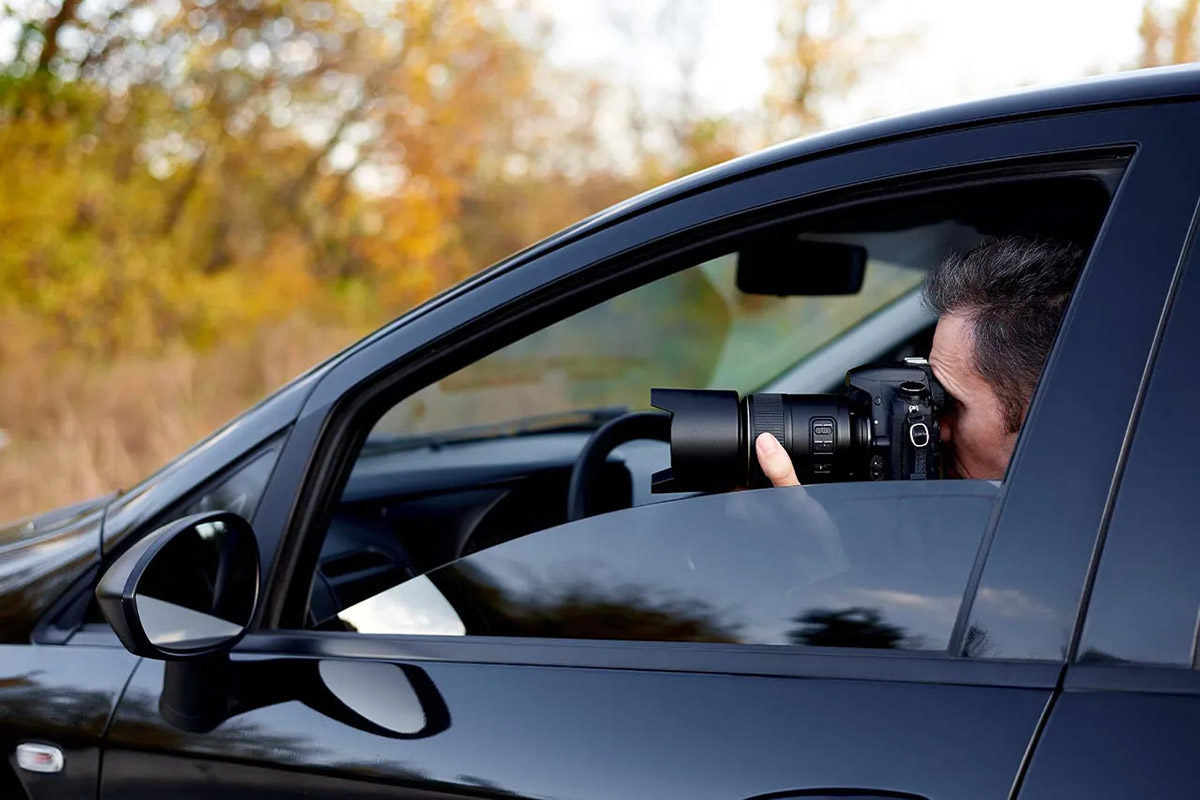 Un investigatore privato in auto impegnato in un pedinamento scatta fotografie