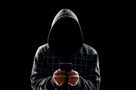 Un uomo incappucciato tiene in mano un telefono sotto controllo