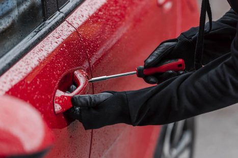 Un ladro tenta di forzare la portiera di un auto con un cacciavite per tentare un furto