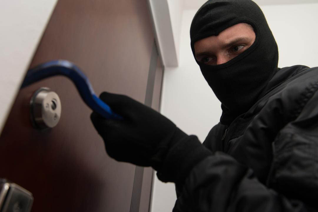 Un ladro tenta di forzare la porta di accesso a un appartamento con un piede di porco